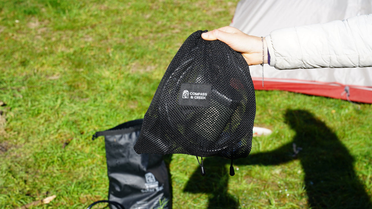 Compass & Creek mesh bag packed with the shower pump kit at a campsite, with the Solar Sac beside it